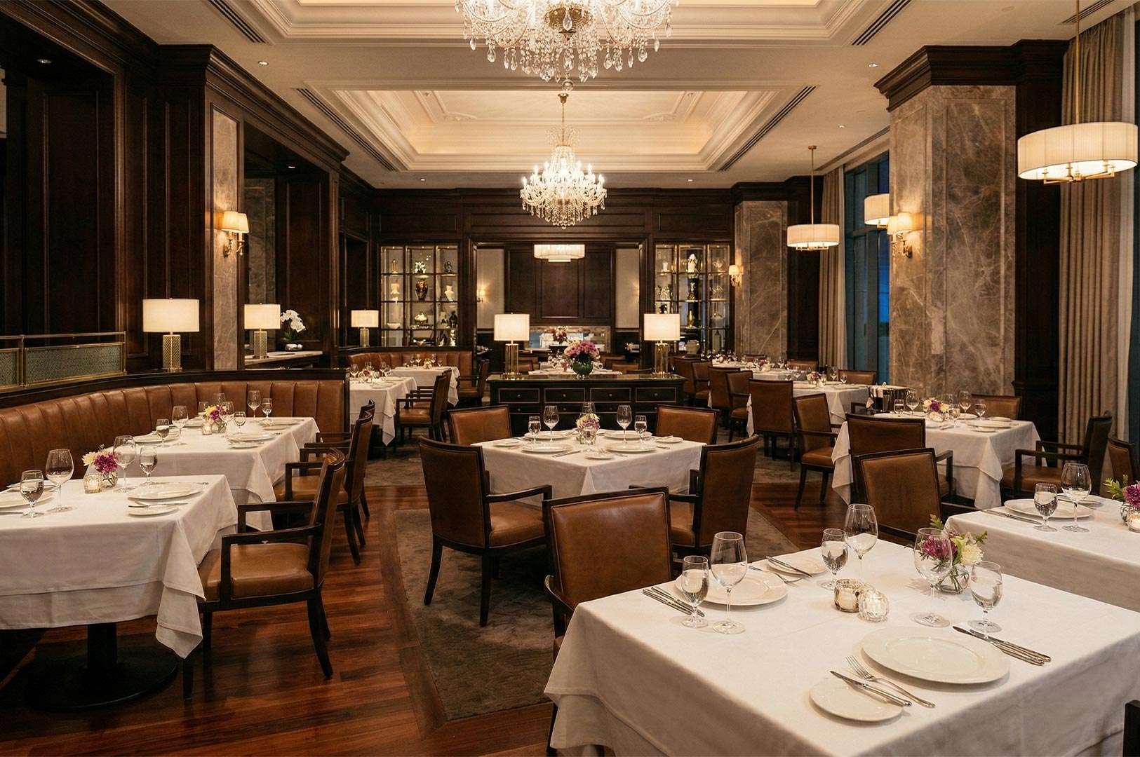 Elegant fine dining room with white tablecloths, leather chairs, crystal chandeliers, and warm ambient lighting.