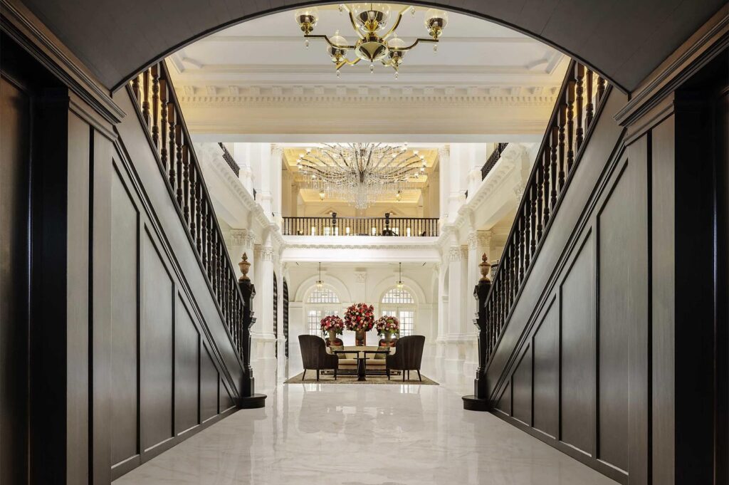Symmetrical view of a grand hotel lobby featuring dark wood staircases, white marble floors, and a massive crystal chandelier.