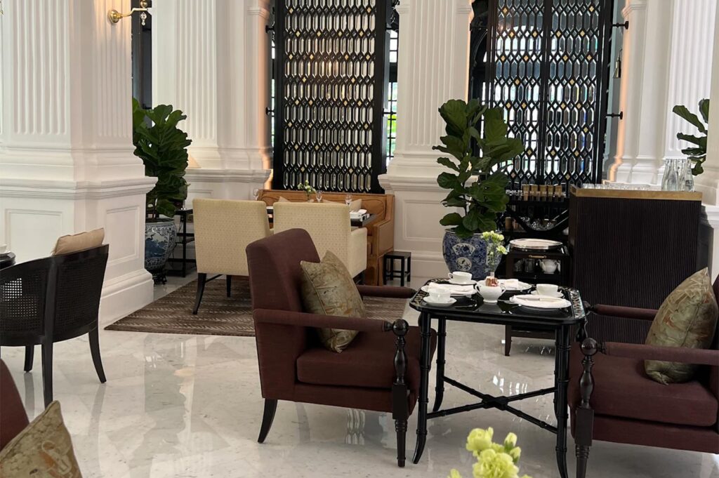 Elegant lounge area with plush velvet armchairs, marble floors, and white fluted columns, set for afternoon tea.