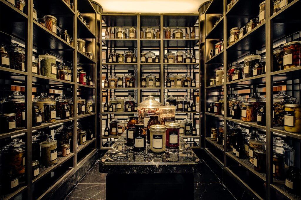 A symmetrical view of a floor-to-ceiling ingredients room filled with glass jars containing dried herbs, spices, and garnishes.