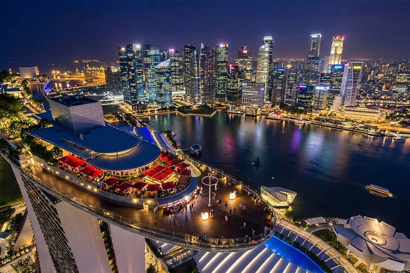 Aerial night view of Marina Bay Sands SkyPark rooftop deck overlooking the illuminated Singapore city skyline and Marina Bay.