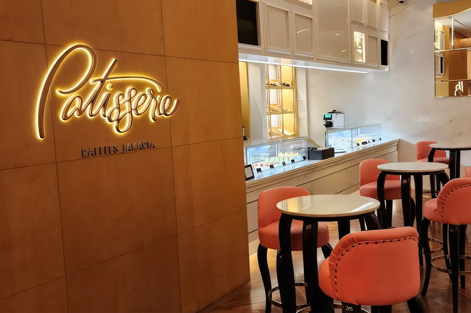 Cozy patisserie interior with warm lighting. Elegant round tables, coral-pink chairs, and a stylish wall sign create an inviting atmosphere.