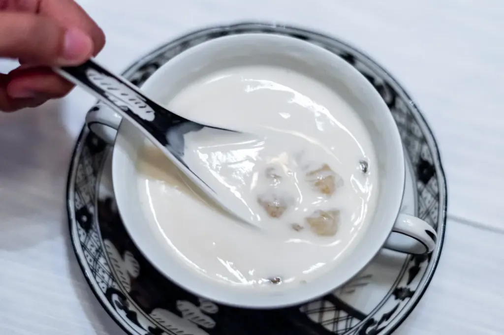 A close-up of a traditional Cantonese coconut milk soup with soft taro chunks, being served with a black and white patterned ceramic spoon.