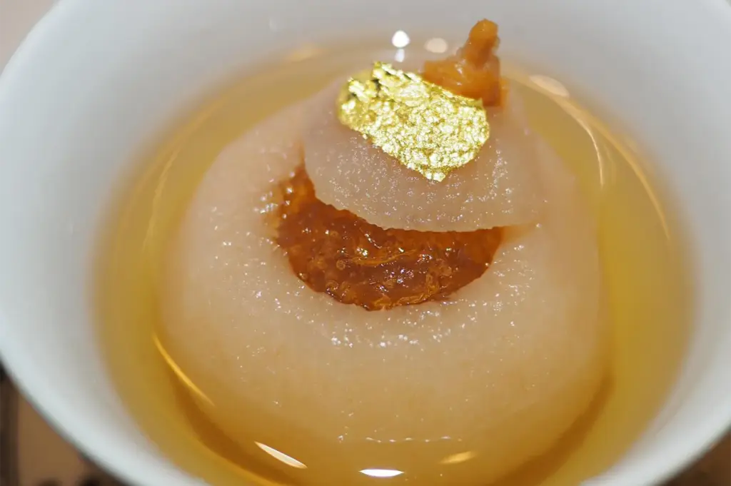 A luxury Chinese dessert of double-steamed snow pear filled with peach gum or bird's nest, garnished with edible gold leaf in a clear syrup.