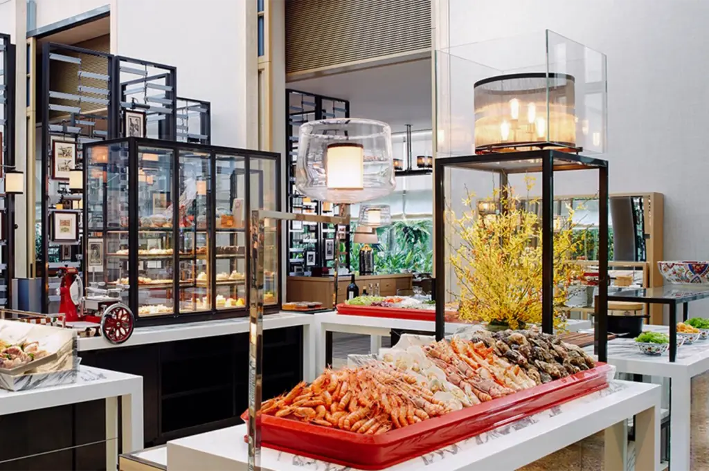 A lavish seafood buffet display featuring fresh prawns, oysters, and crab legs in a high-ceilinged, bright dining hall.