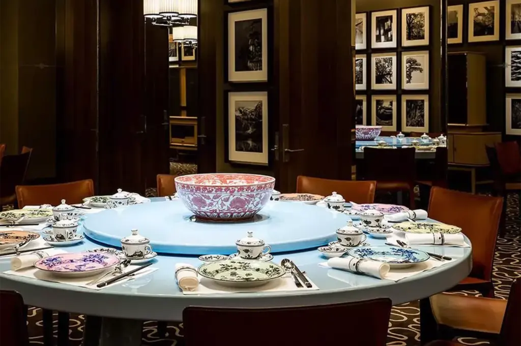 A private dining room set for a large group featuring a light blue Lazy Susan turntable and ornate porcelain tableware.