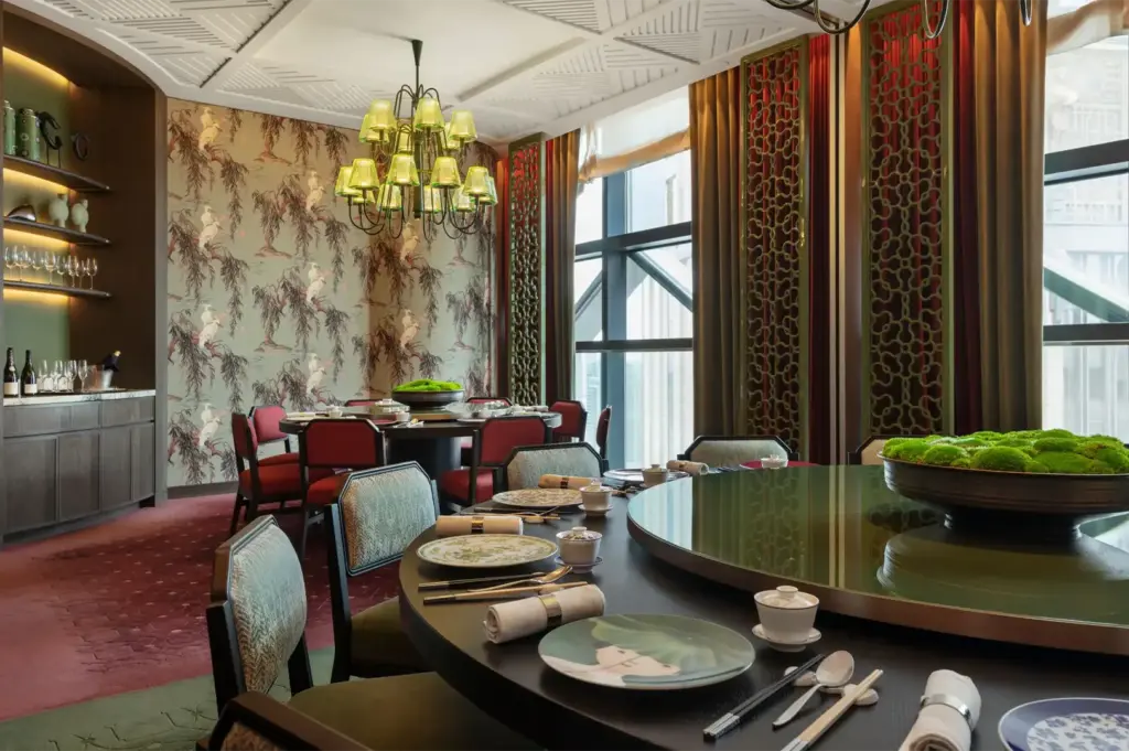 A luxury private banquet room with bird-themed wallpaper, green chandeliers, and two large round tables set for a formal dinner.