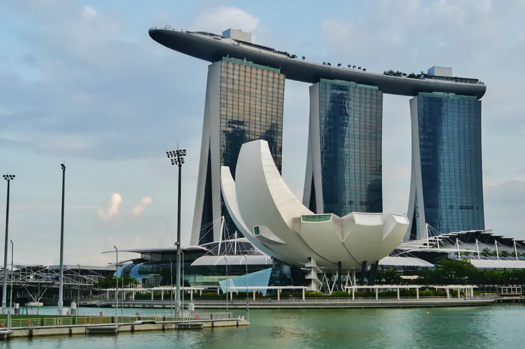 An exterior wide shot of the Marina Bay Sands hotel towers and the lotus-shaped ArtScience Museum in Singapore under a blue sky.