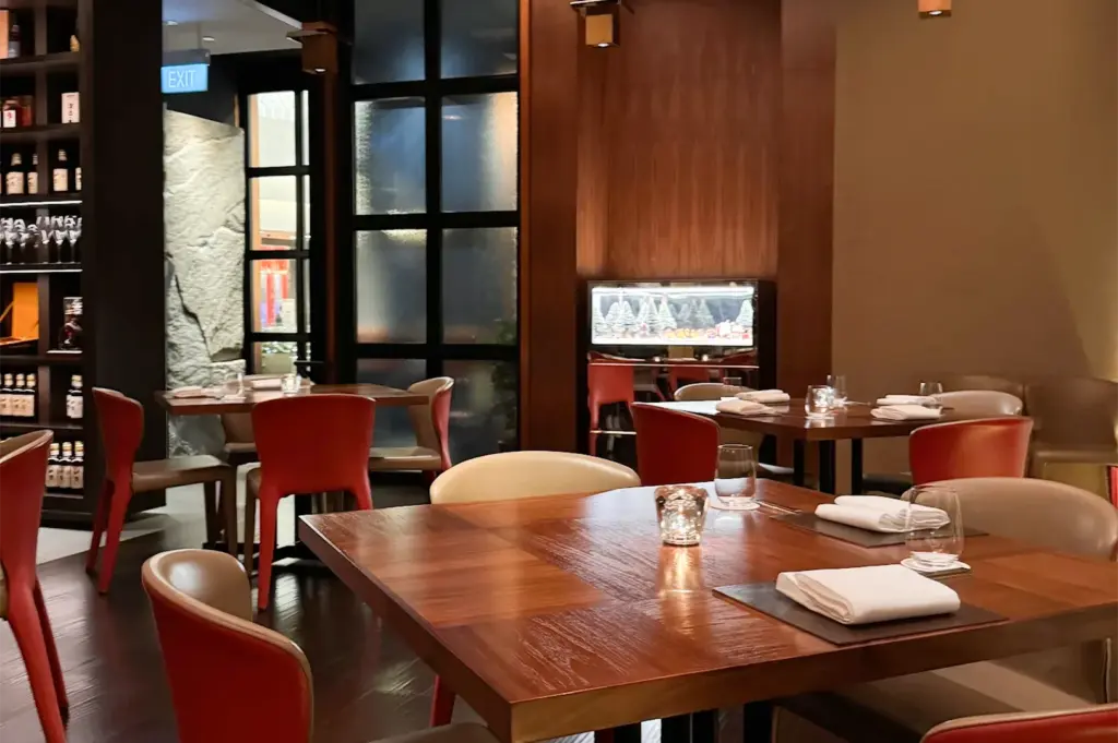 Elegant interior of a fine dining restaurant featuring dark wood tables, red leather chairs, and warm ambient lighting.