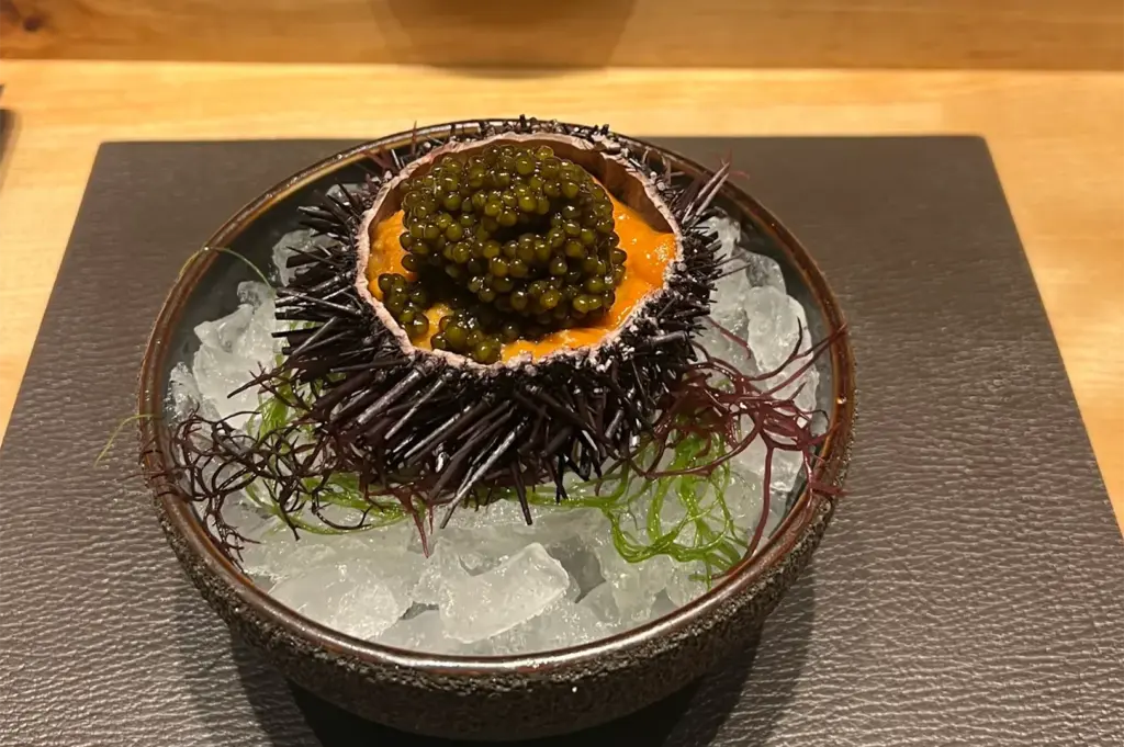 A gourmet appetizer of fresh orange sea urchin (uni) topped with black caviar, served in a spiny shell over crushed ice.