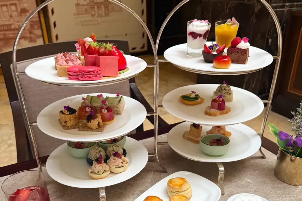 A close-up of a three-tier silver afternoon tea stand filled with colorful gourmet pastries, savory sandwiches, macarons, and fresh scones.