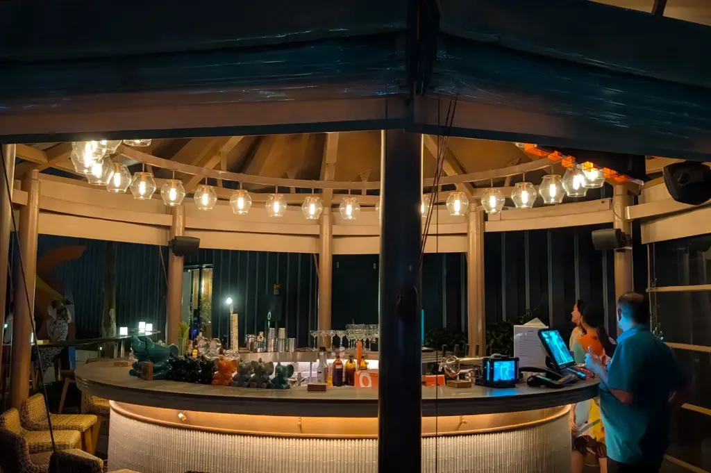 Elegant circular bar at Mr. Stork, Andaz Singapore, featuring a warm bronze bar countertop ambient backlighting, and a variety of premium spirits, set against a backdrop of lush rooftop greenery.