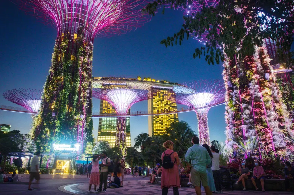 Illuminated Supertree Grove at Gardens by the Bay in Singapore at night with colorful lights and Marina Bay Sands in the background.
