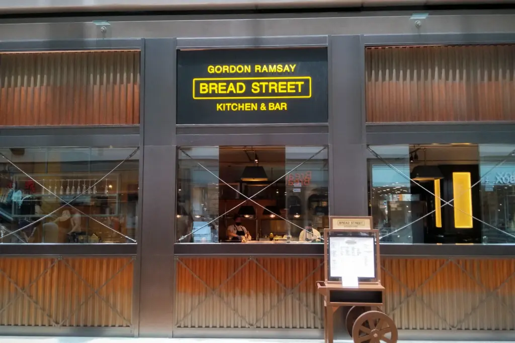 Front entrance of Gordon Ramsay Bread Street Kitchen & Bar in Singapore with illuminated restaurant signage and modern interior dining area visible through glass windows