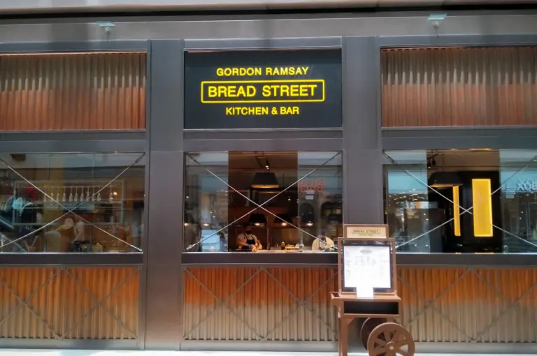 Front entrance of Gordon Ramsay Bread Street Kitchen & Bar in Singapore with illuminated restaurant signage and modern interior dining area visible through glass windows