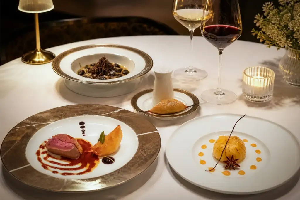 Elegant fine dining table setting at Les Amis Singapore featuring a curated tasting menu with plated duck, gourmet dessert, and truffle dish, styled with wine glasses and warm ambient lighting in a refined restaurant atmosphere