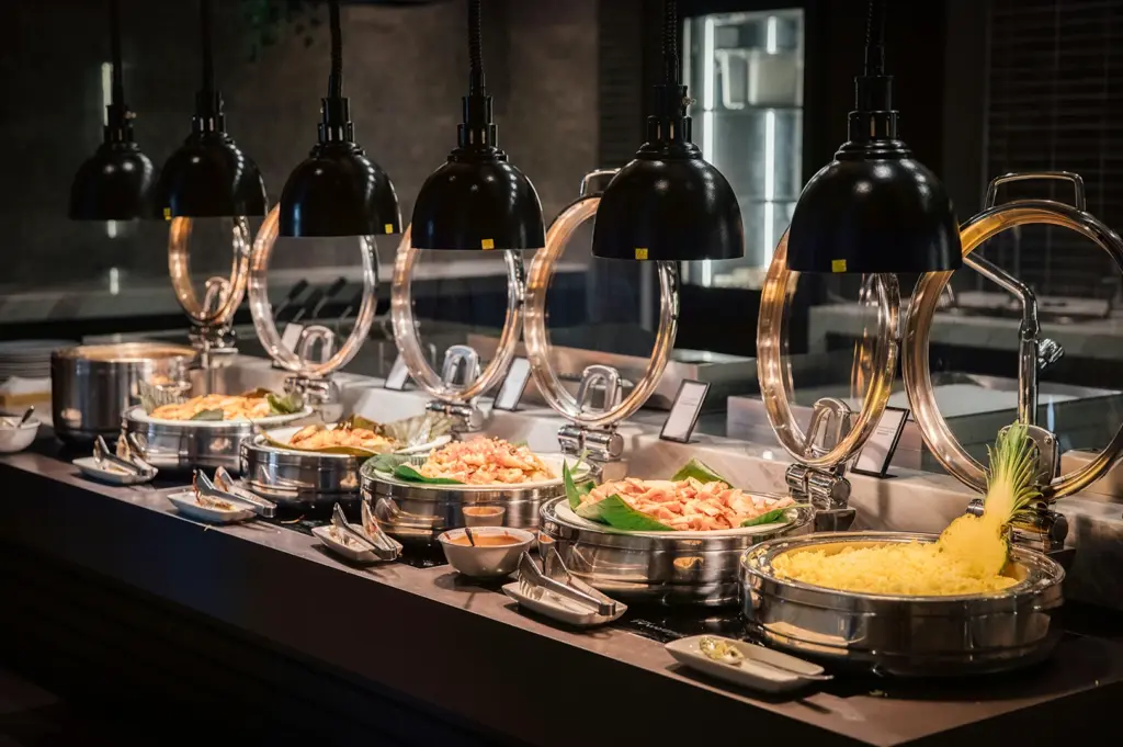 Elegant buffet dining station with stainless steel chafing dishes under warm pendant lights featuring assorted hot dishes in a modern restaurant interior