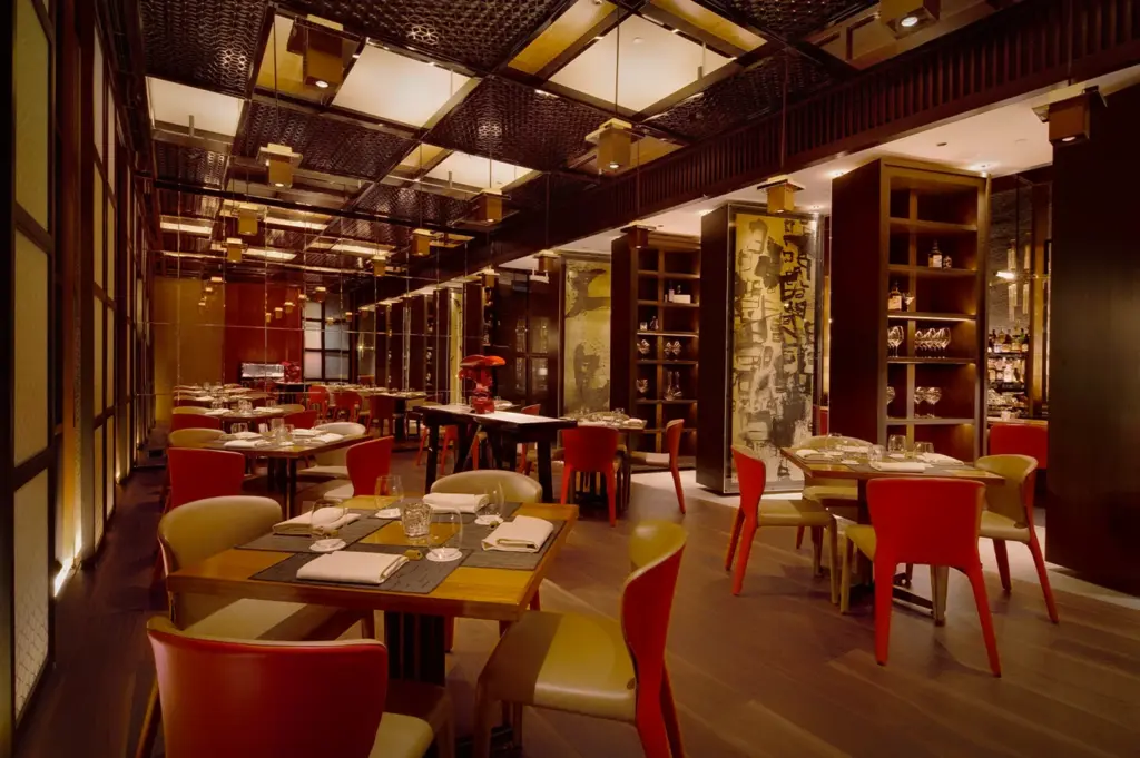 Elegant interior dining space of Waku Ghin restaurant in Singapore featuring warm ambient lighting, modern Japanese-inspired decor, polished wood finishes and red upholstered chairs arranged around fine dining tables
