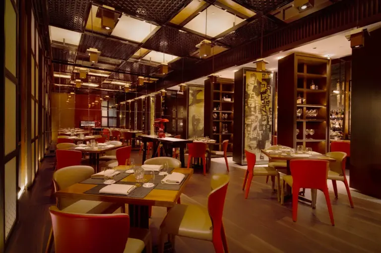 Elegant interior dining space of Waku Ghin restaurant in Singapore featuring warm ambient lighting, modern Japanese-inspired decor, polished wood finishes and red upholstered chairs arranged around fine dining tables
