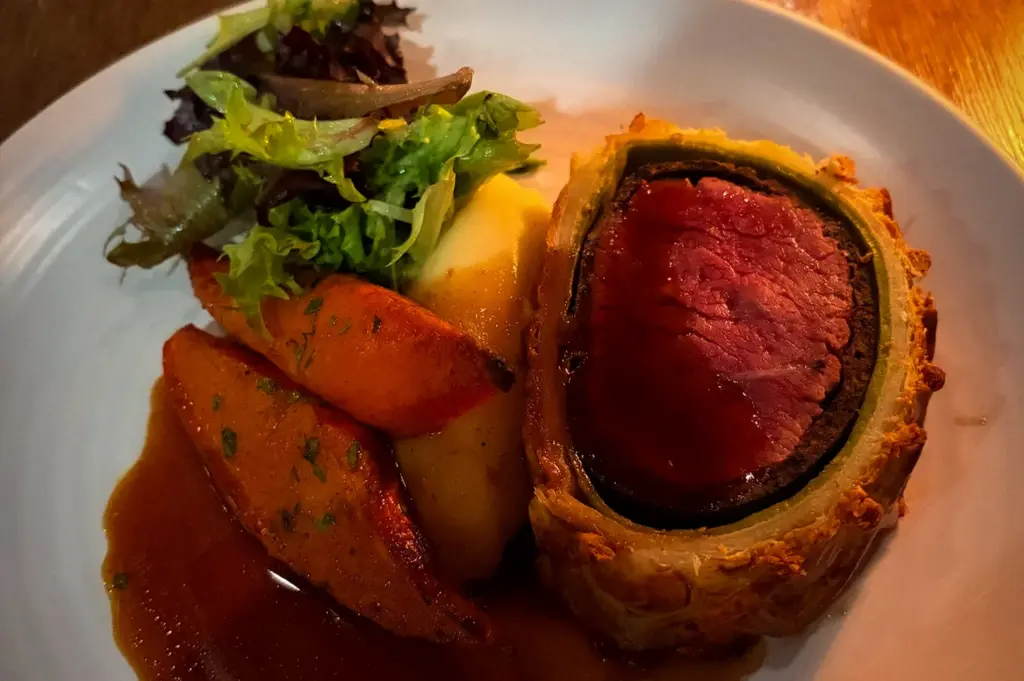 Beef Wellington served at Bread Street Kitchen Singapore with roasted potatoes, mixed greens, and rich brown sauce on a white dinner plate under warm restaurant lighting