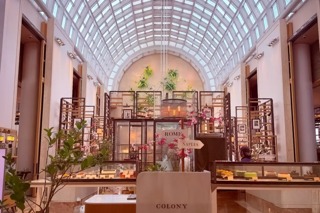 Elegant interior of Colony restaurant at The Ritz-Carlton Millenia Singapore, featuring a vaulted glass ceiling, luxury dessert displays, and signature colonial-inspired decor.