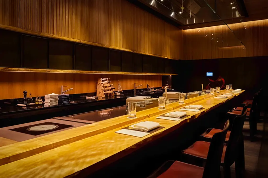 Minimalist chef’s table dining counter at Waku Ghin in Singapore featuring warm wooden interiors, intimate omakase-style seating and elegant fine dining presentation setup under ambient lighting