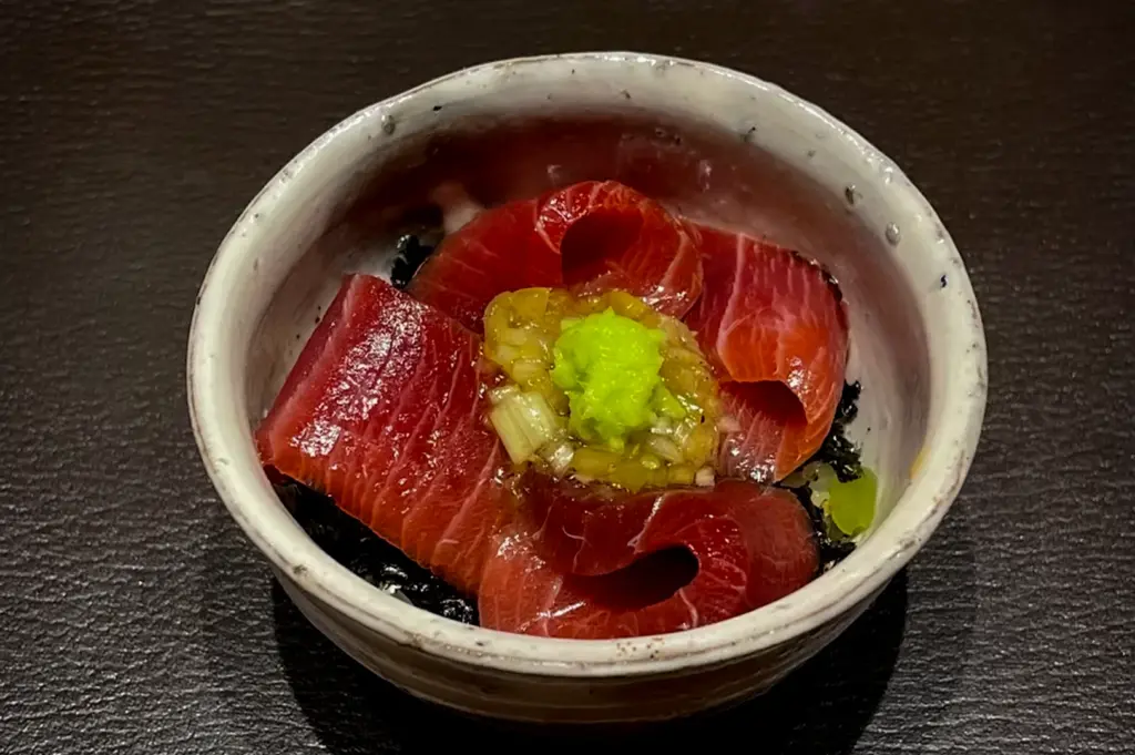 Premium tuna sashimi bowl at Waku Ghin Singapore featuring fresh marbled tuna slices topped with wasabi, soy-marinated garnish and seaweed served in a minimalist Japanese ceramic bowl
