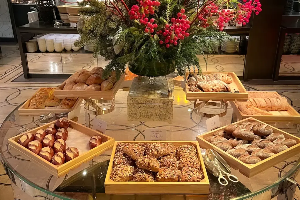 A variety of freshly baked artisanal breads and rolls, including multigrain and pretzels, displayed in wooden trays at the Colony restaurant buffet in Singapore