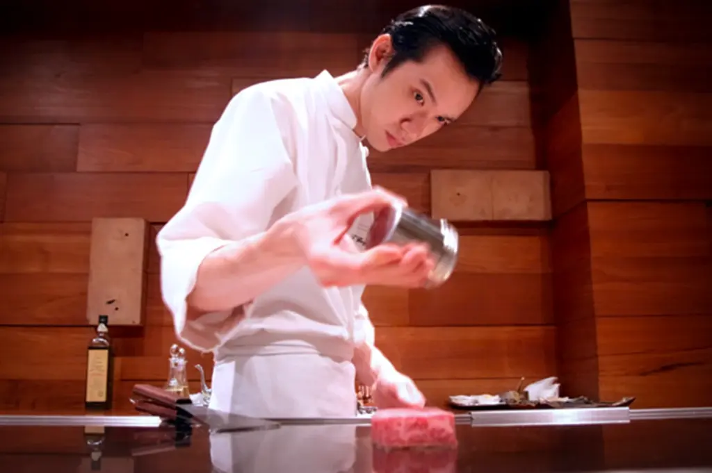 Chef preparing premium wagyu beef at Waku Ghin Singapore inside an intimate Japanese fine dining counter with warm wooden interiors and teppanyaki-style presentation