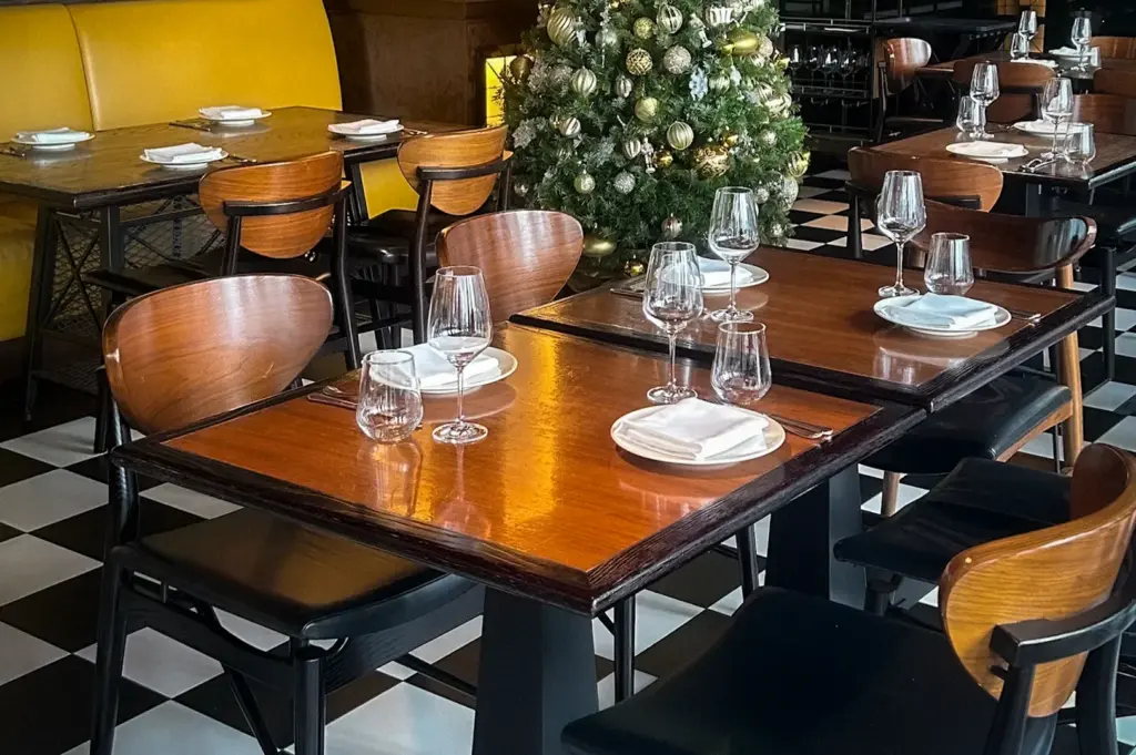 Dining area interior of Bread Street Kitchen Singapore with wooden tables, checkered flooring, modern hanging lights, and a decorated Christmas tree in the restaurant seating area