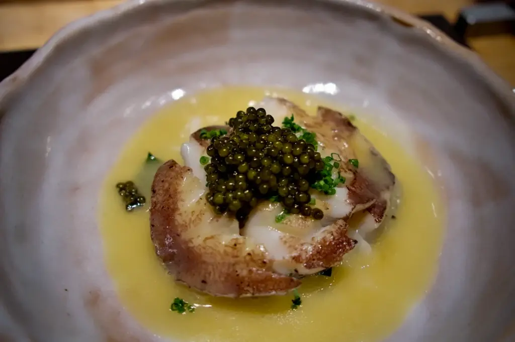 Refined seafood course at Waku Ghin Singapore featuring lightly seared shellfish topped with premium caviar in a creamy sauce served in an artisanal Japanese ceramic bowl at the chef’s counter