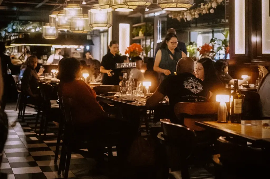 Busy dinner service at Bread Street Kitchen Singapore featuring warm ambient lighting, checkered flooring, modern hanging lamps, and diners seated inside the stylish restaurant interior